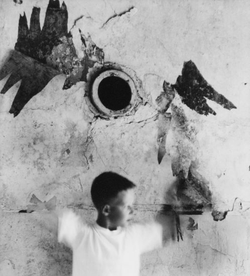 A black and white photograph of a young boy in motion against a distressed wall.