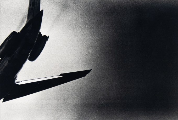 A black and white photograph of the tail of a plane seen from below.