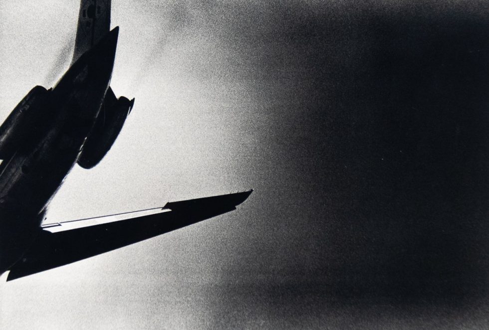 A black and white photograph of the tail of a plane seen from below.