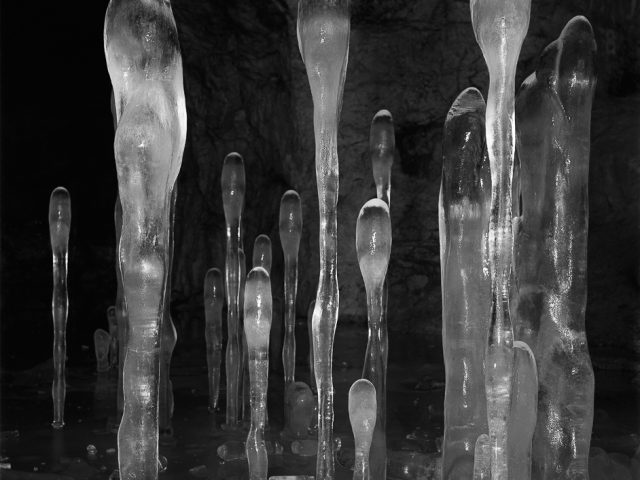 A black and white photograph of frozen stalagmites in a cave-like setting.