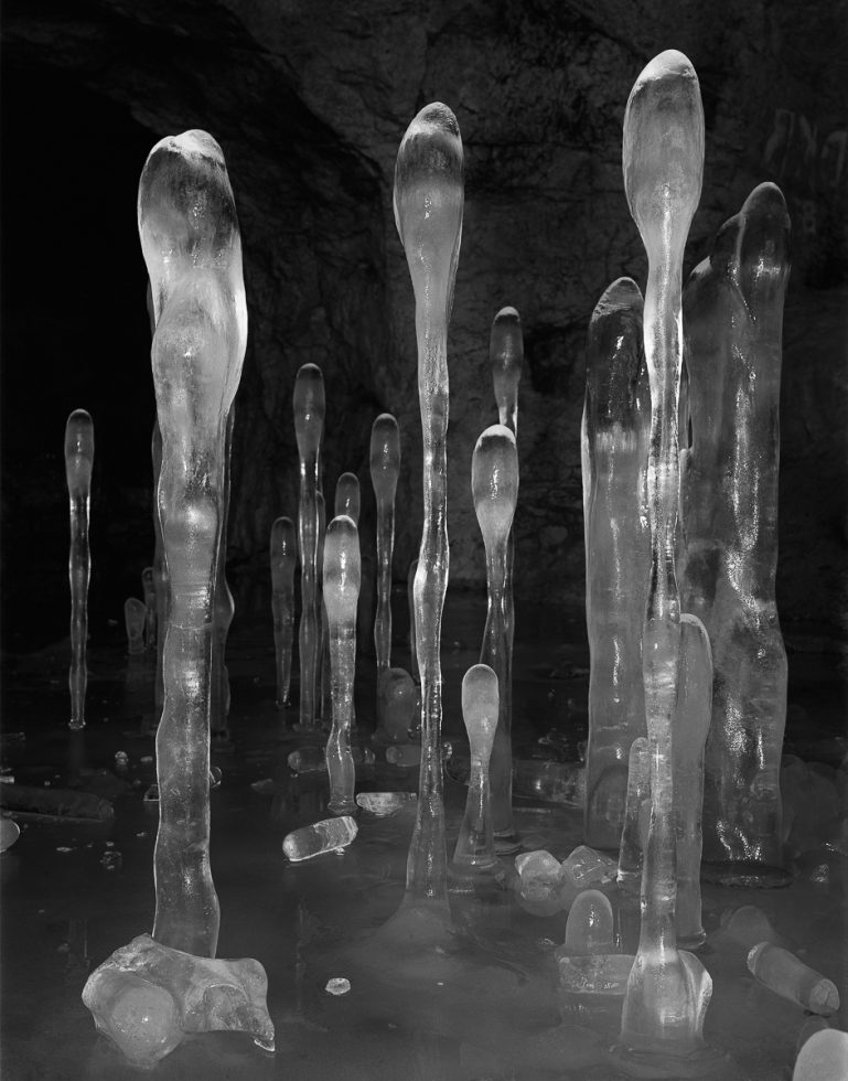 A black and white photograph of frozen stalagmites in a cave-like setting.