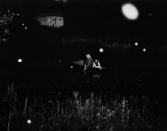 A black and white photograph of two people in a boat on a pond at night.
