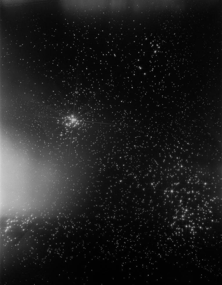 A black and white photograph of the night sky with many stars shining.