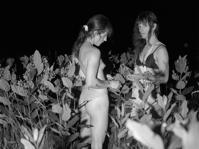 A black and white photograph of two women standing in a field at night facing each other.