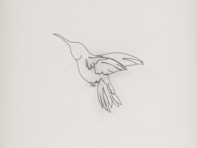 A humming bird silhouette made of wire against a white paper background.