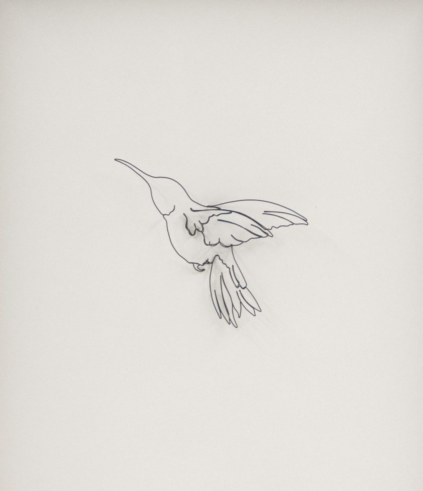 A humming bird silhouette made of wire against a white paper background.