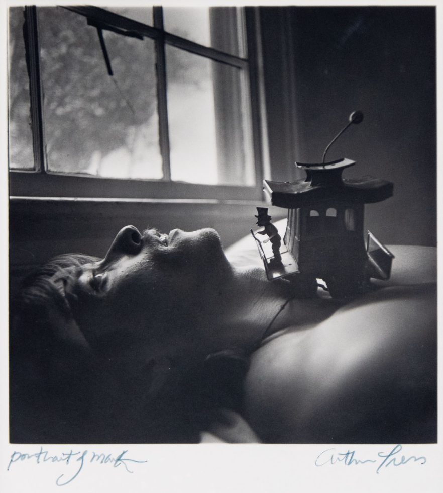 A black and white portrait of a man laying on his back next to a window.