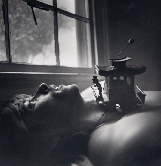 A black and white portrait of a man laying on his back next to a window.