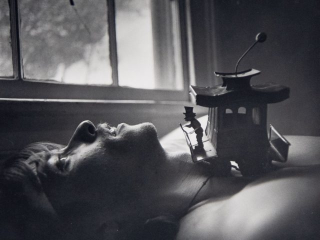 A black and white portrait of a man laying on his back next to a window.