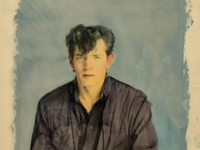 A hand-colored photograph of a man with yellow skin against a blue background.