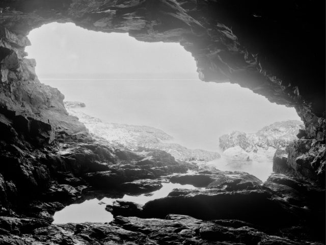 A black and white photograph of a view outside of a cave.