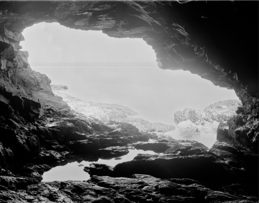 A black and white photograph of a view outside of a cave.