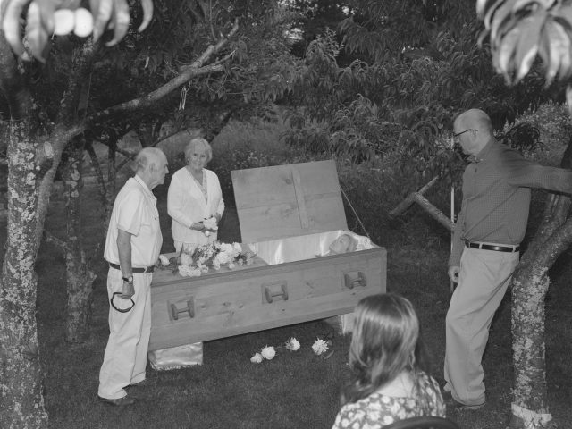 A black and white photograph of a funeral in an orchard.
