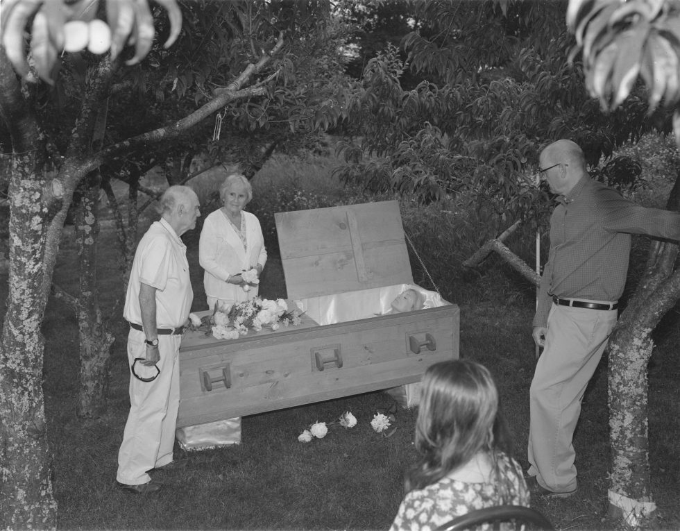 A black and white photograph of a funeral in an orchard.