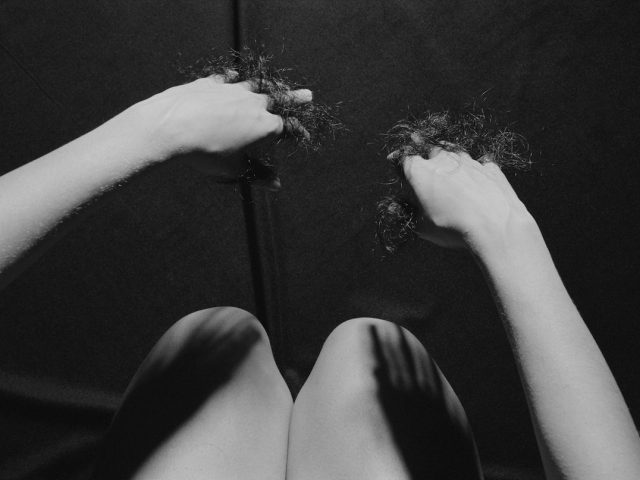 A black and white photograph of a woman with hair between her fingers.