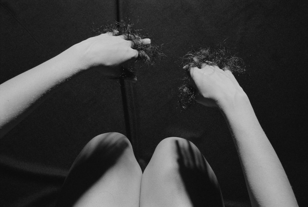 A black and white photograph of a woman with hair between her fingers.