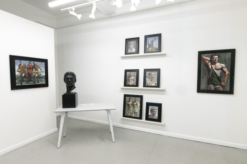 This image shows the walls of a gallery where eight framed paintings hang. On a table, a black statue of a man's head is displayed.