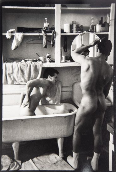 A black-and-white photograph of two men getting ready in a small bathroom.
