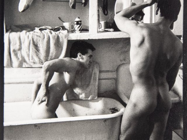 A black-and-white photograph of two men getting ready in a small bathroom.