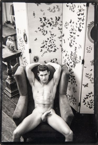 A black-and-white photograph of a nude man in an easy chair seen from above.