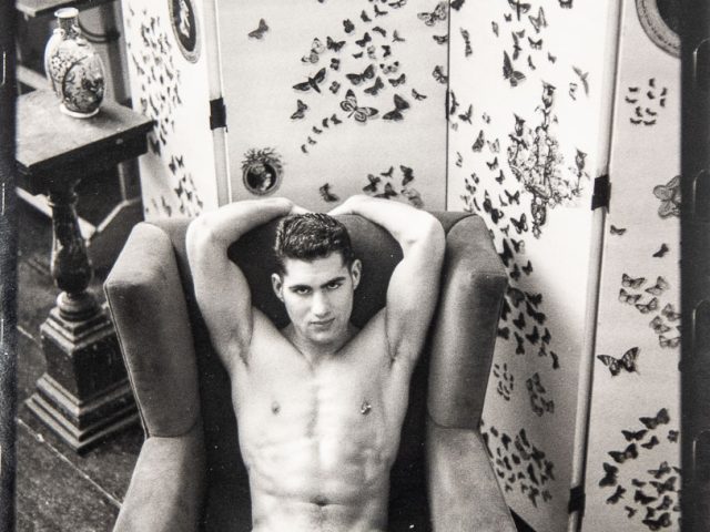 A black-and-white photograph of a nude man in an easy chair seen from above.