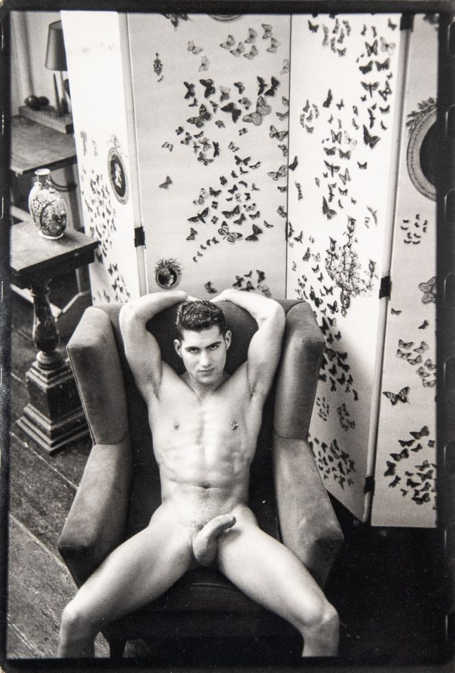 A black-and-white photograph of a nude man in an easy chair seen from above.