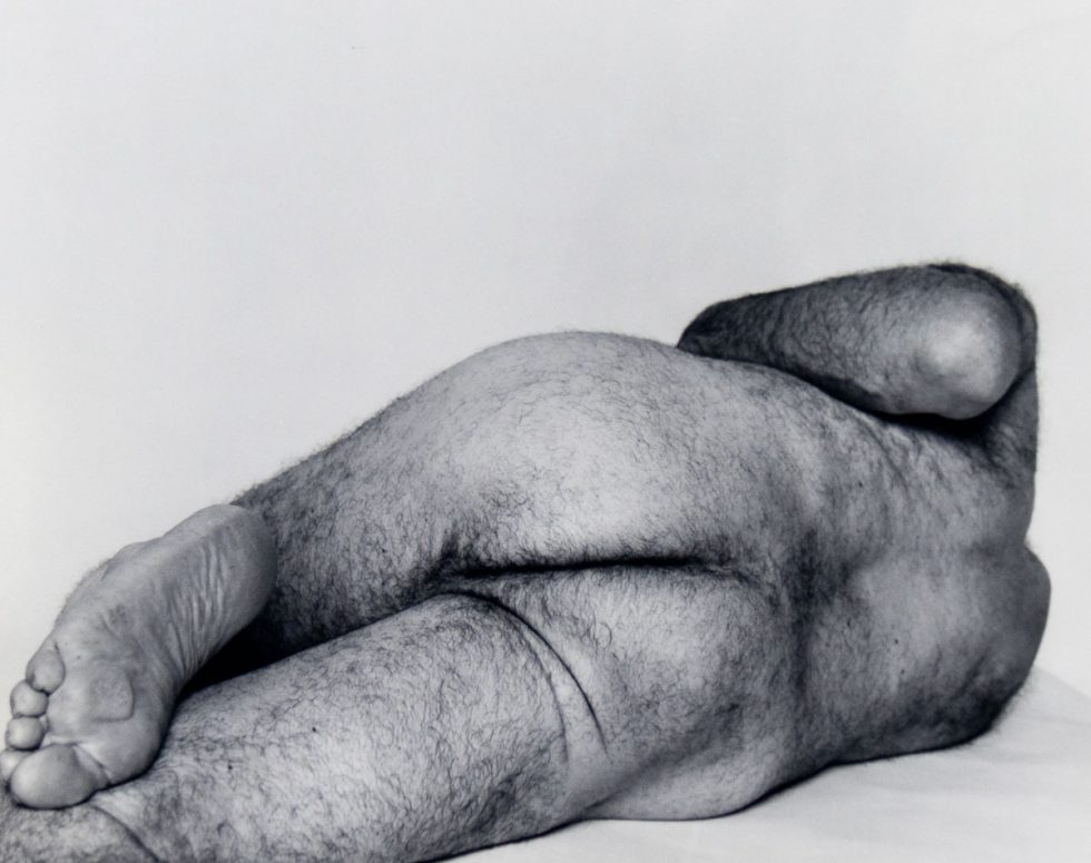 A black and white photograph of a male nude reclining.