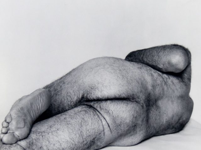 A black and white photograph of a male nude reclining.