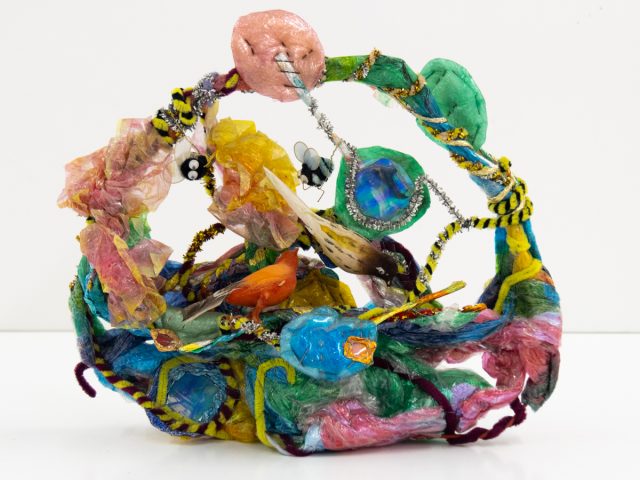 A bright sculpture depicting a basket with birds, bees, and candy.