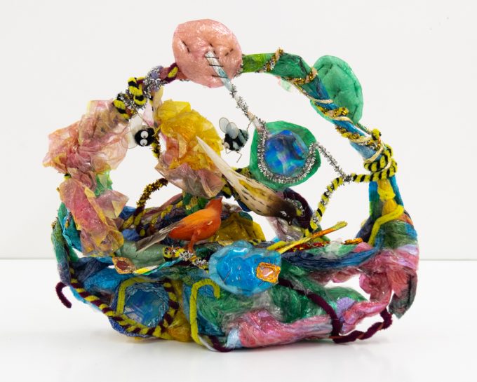 A bright sculpture depicting a basket with birds, bees, and candy.