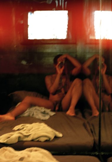 A colorful mirror selfie of a nude man sitting on the floor.