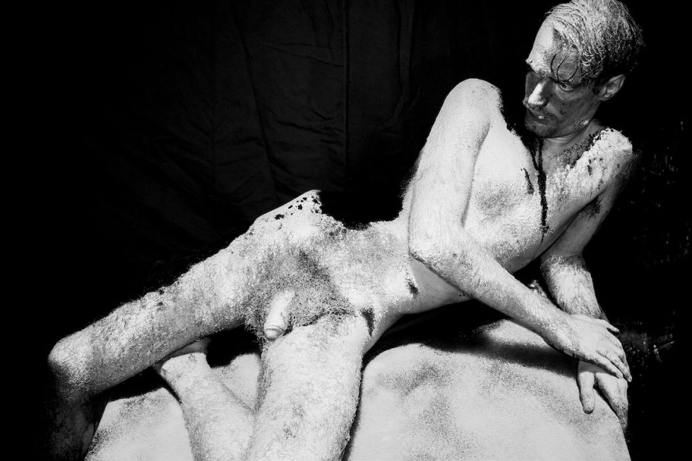 A black and white image of a nude man lying on his side.
