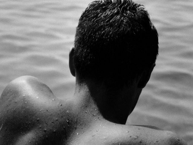 A black and white photograph of the back of a man's head by the water.