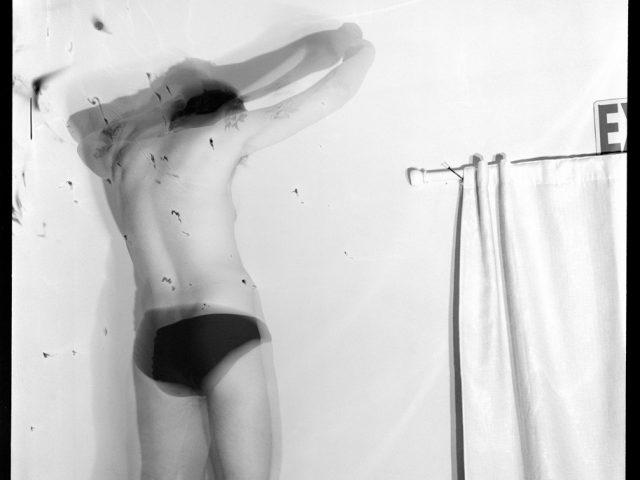 A black and white photograph of a man in black underwear.