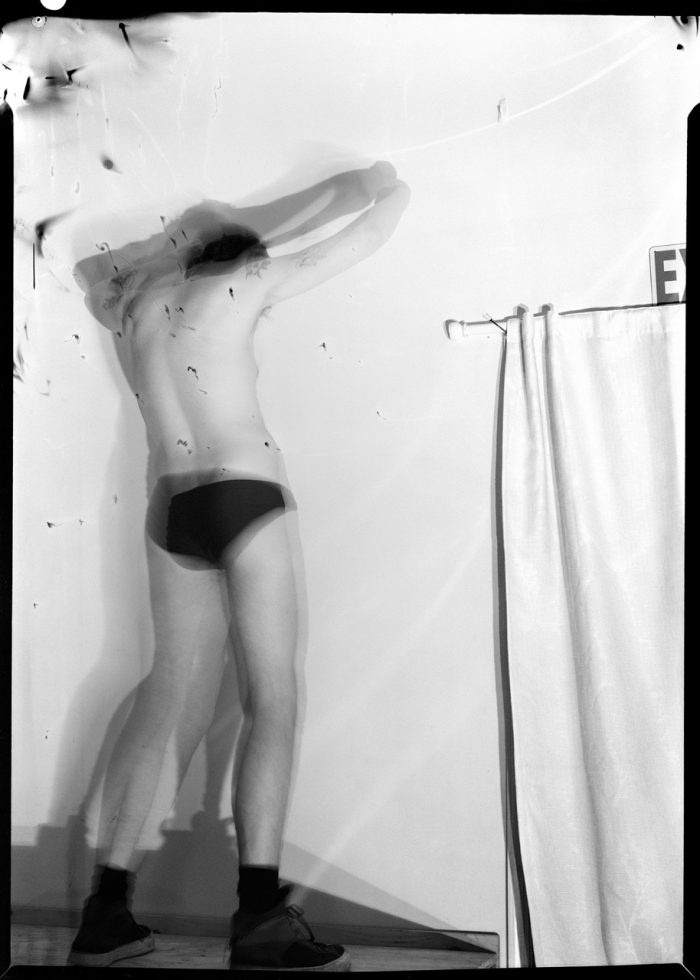 A black and white photograph of a man in black underwear.