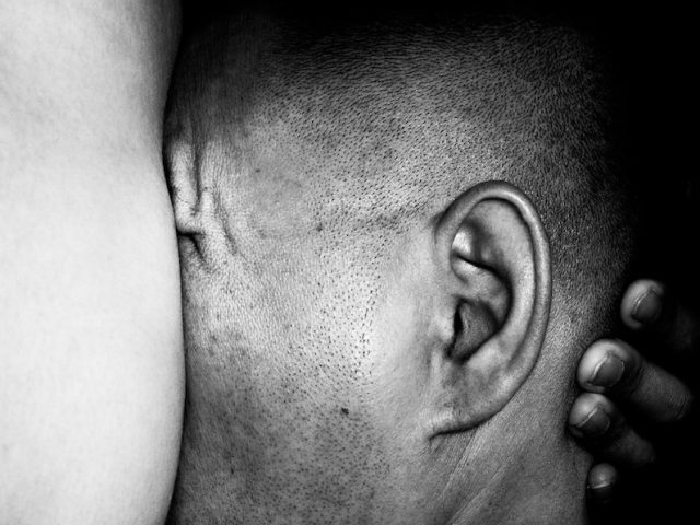 A black and white photograph of a head pressed up against breasts.