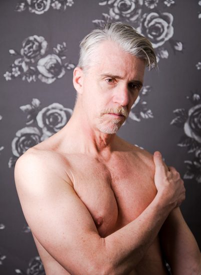 A color photograph of a shirtless man with silver hair.