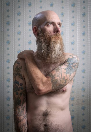 A color photograph os a shirtless man with a long beard.