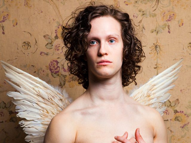 A color photograph os a shitless man with white wings.