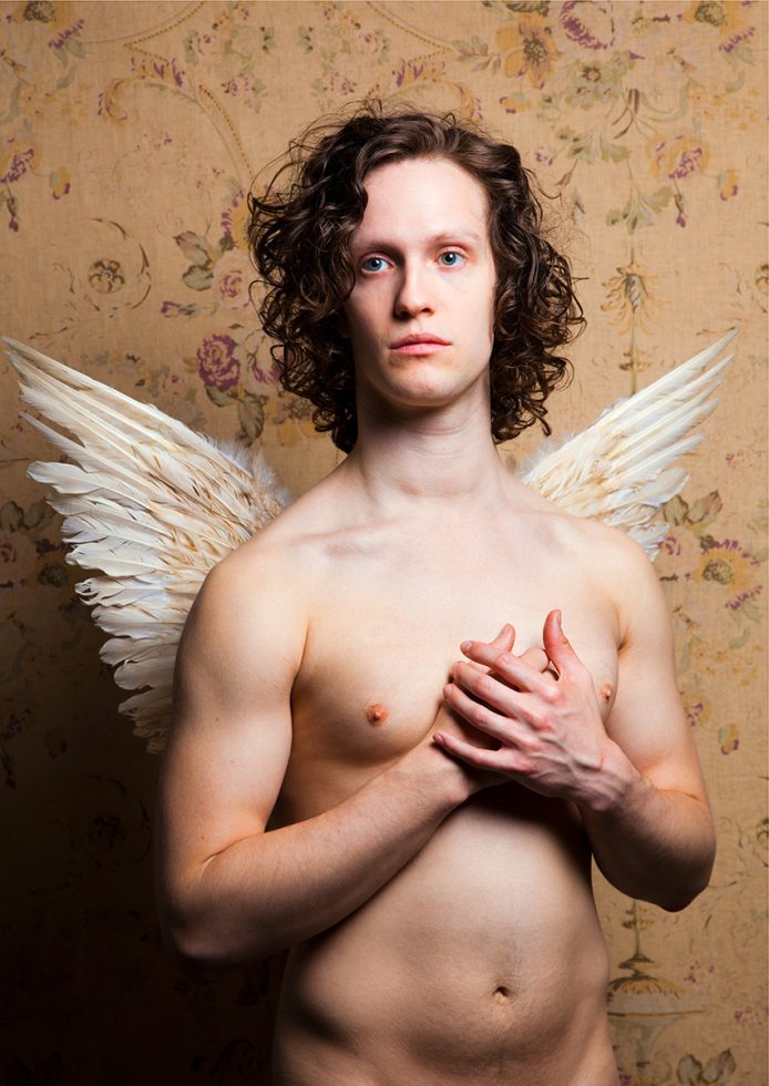 A color photograph os a shitless man with white wings.