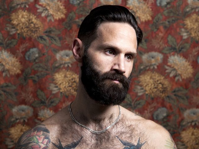 A color photograph os a shirtless hairy man with tattoos.