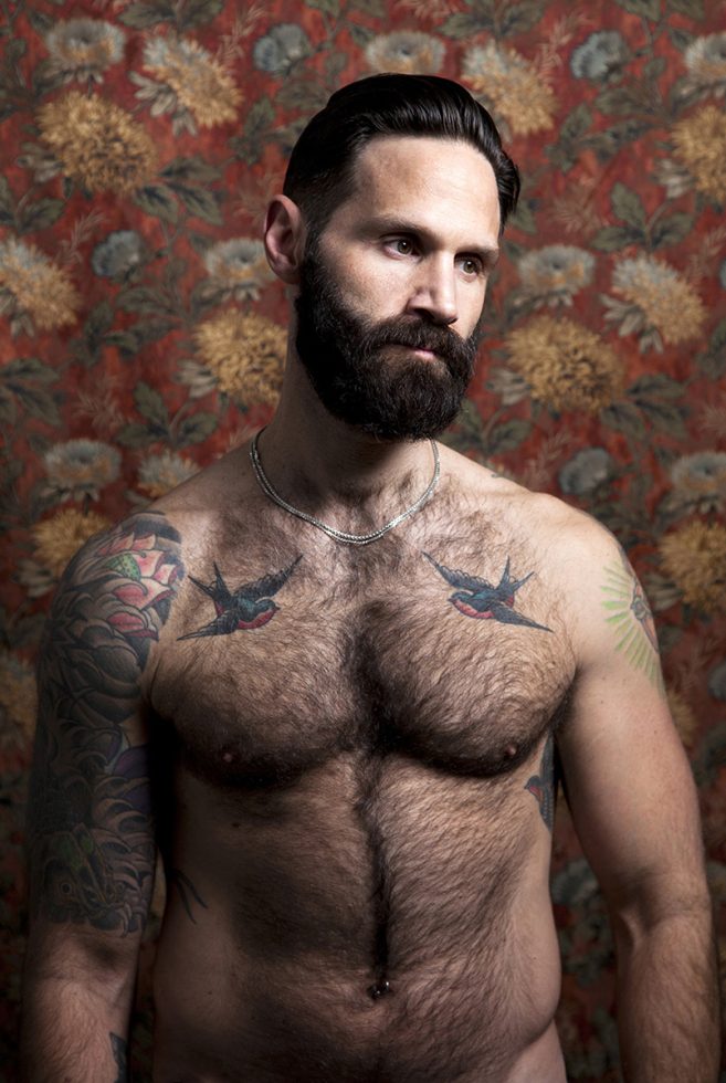 A color photograph os a shirtless hairy man with tattoos.