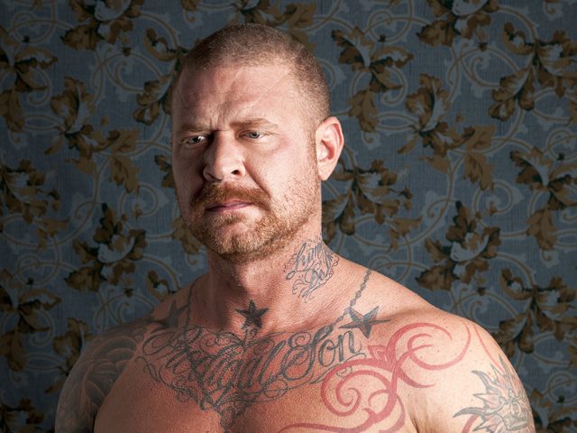 A color photograph of a muscled shirtless man with tattoos.