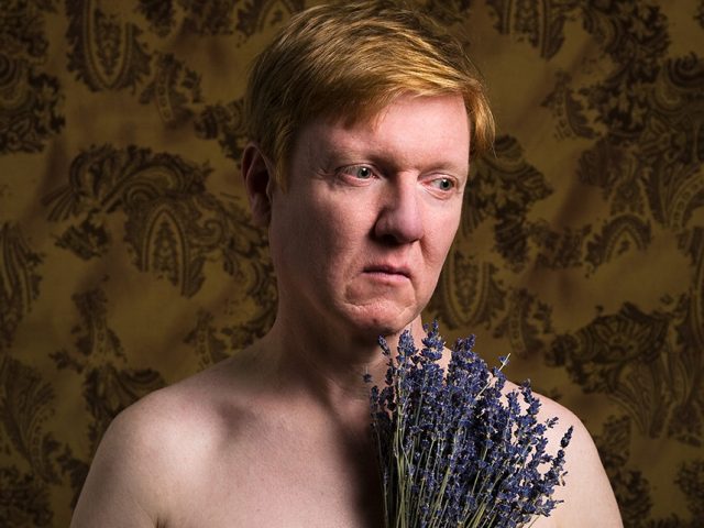 A color portrait of a person holding lavender flowers.