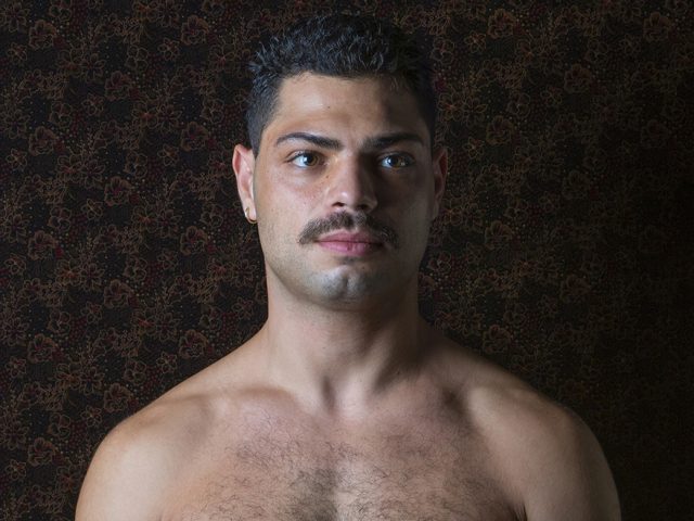A color photograph os a shirtless man with a mustache.