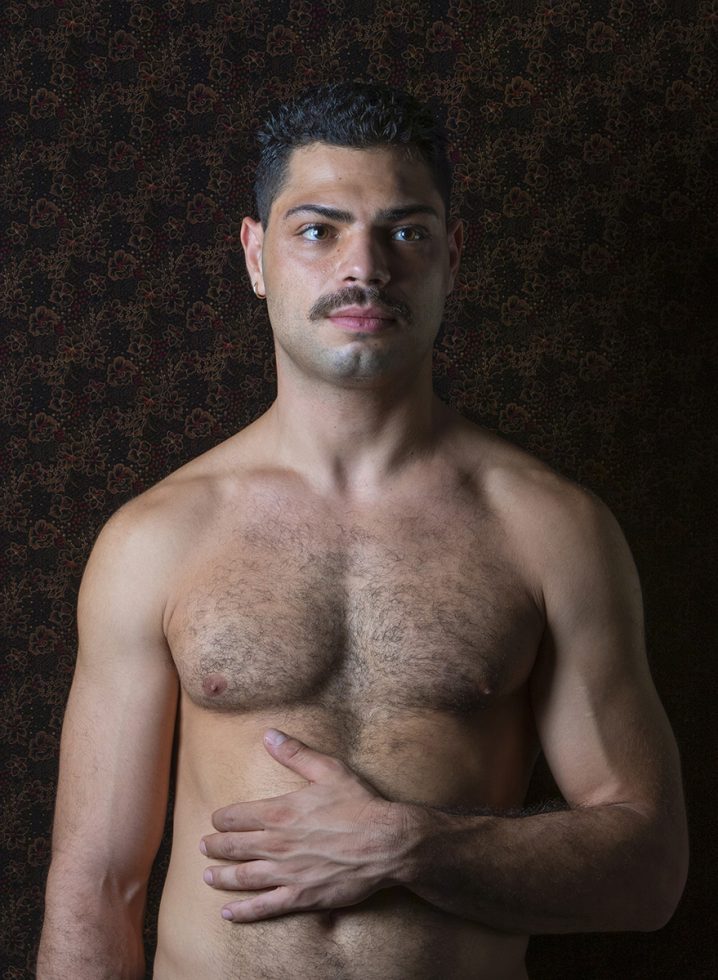 A color photograph os a shirtless man with a mustache.