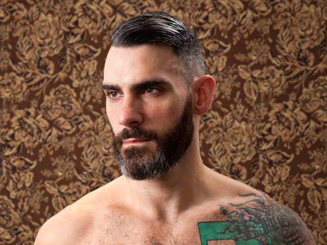 A color photograph of a shirtless man with a beard.