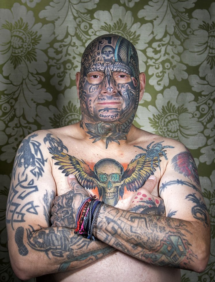 A color photograph os a shitless man with tattoos.