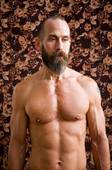 A color photograph of a shirtless man with a beard.