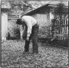 A black and white photograph of a man bent forward in a yard.